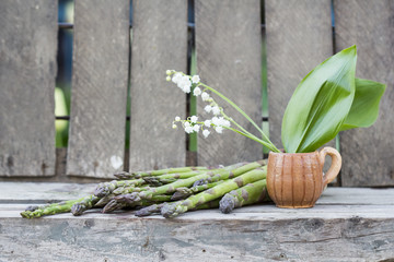 Still life composition with asparagus and ceramic pot with lily-of-the-valley flowers on wooden background