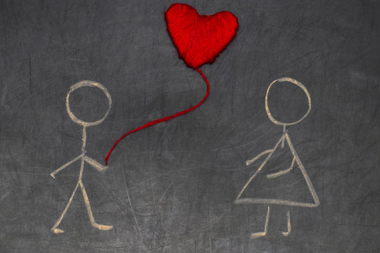 Couple in love drawing with chalk on the chalkboard and red hear