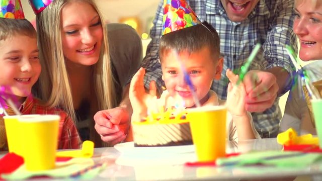 Kid birthday celebration. Little boy blows out candles on birthday cake at party, Happy big family celebrating birthday of kid. slow motion 240 fps, high speed camera, HD 1080p