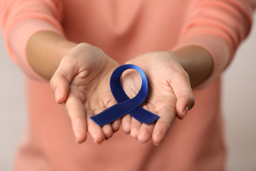 Close up view of female hands holding blue ribbon. Colon cancer concept