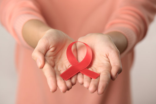 Close up view of female hands holding red ribbon. Aids concept