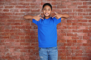 Young African American boy in blank blue t-shirt standing against brick wall