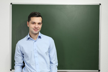 Handsome young teacher near blackboard in classroom