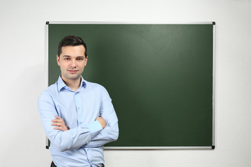 Handsome young teacher near blackboard in classroom