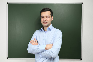 Handsome young teacher near blackboard in classroom