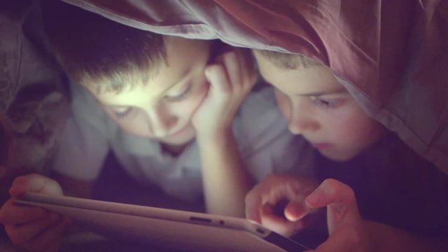 Two kids using tablet pc under blanket at night. Brothers with tablet computer in a dark room. Slow motion HD 1080p