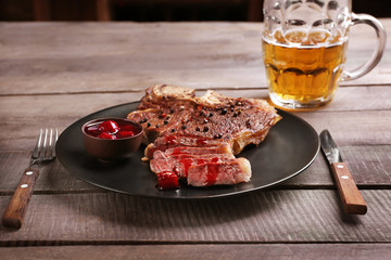 Grilled steak on plate and mug of beer on wooden background