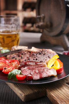 Grilled steak with fresh vegetables on plate and mug of beer on wooden table