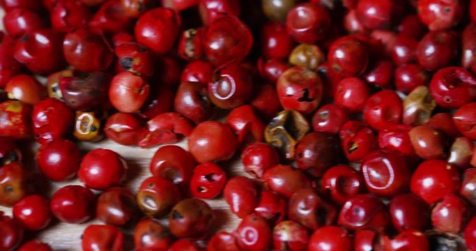 grains of pepper pink pepper colorful in extreme slow-motion fall on a wooden surface and mingle with each other 