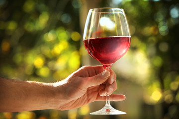 Male hand holding glass with wine on blurred natural background