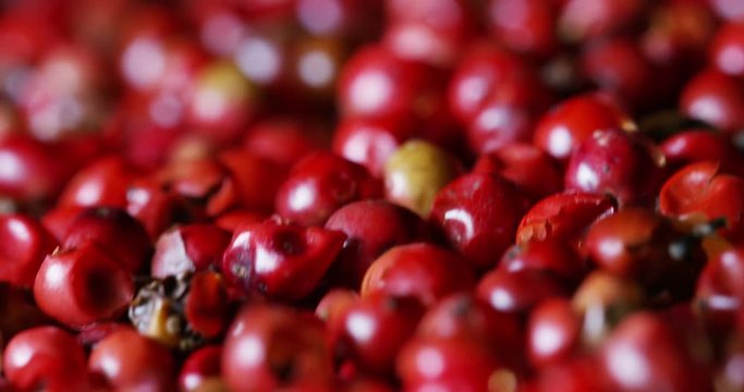 grains of pepper pink pepper colorful in extreme slow-motion fall on a wooden surface and mingle with each other 