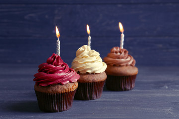 Tasty chocolate cupcakes with candles on wooden table against dark background