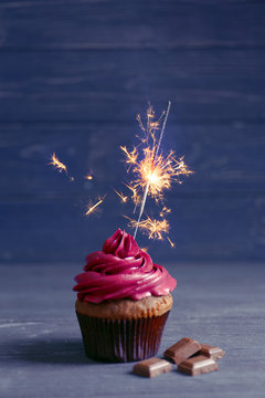 Tasty cupcake with sparkler and chocolate on wooden table against dark background