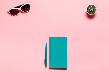 Creative flat lay photo of workspace desk with aquamarine notebook, eyeglasses, cactus copy space pink background, minimal style