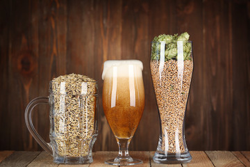 Glasses with beer, hops and malts on wooden background