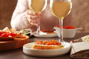 Woman sitting at table with glass of wine and tasty bruschetta