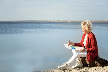 Fototapeta premium Senior female artist painting picture near river