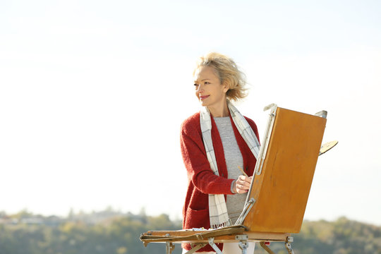 Senior female artist painting picture outdoors