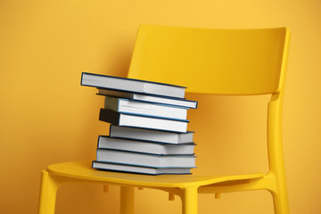 Stack of books on chair on yellow wall background
