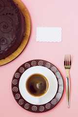 Black coffee whith white card and chocolate cake on pink background