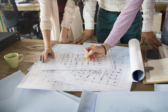 Mid section of architects discussing blueprint in office