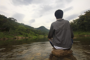 single young man meditate on stone in river on his disappointed holiday (Khiriwong Fuit Village...
