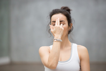 Front view portrait of beautiful young woman wearing white tank top working out against grey wall,...