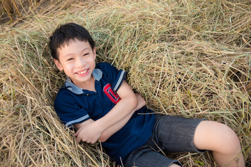 Naklejka na ściany i meble Young asian boy lying on hay and smiles at camera