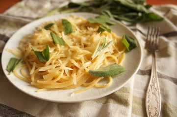 Spaghetti in round white plate with cheese and sage plant on the white and green tablecloth
