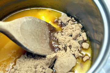 Stirring brown sugar into melted butter with a wooden spoon in a pan on the hob