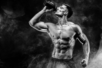 Muscular man with protein drink in shaker over dark smoke background
