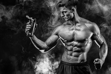 Muscular man with protein drink in shaker over dark smoke background