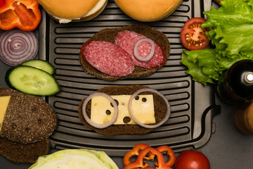 two sandwiches on the grill, vegetables lie around the grill