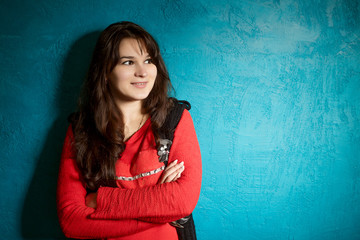 young woman in a beauty blouse and black jacket standing against the backdrop of a blue wall and crossed her arms