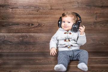 Baby boy smiling on wooden background with bluetooth/wireless headphones.
