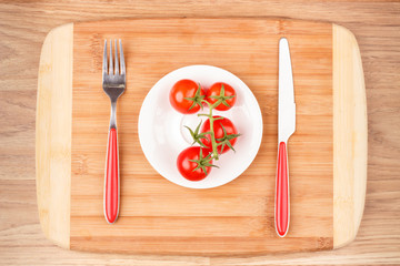 Red fresh raw tomato on the white plate, wooden board