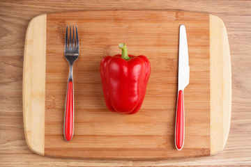 Red fresh raw bell pepper on the white plate, wooden board
