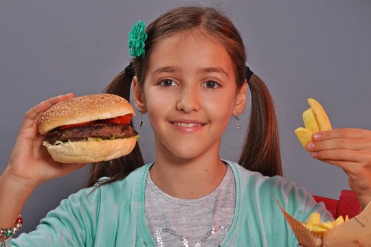 Retrato de una niña comiendo hamburguesa y patatas fritas con refresco.