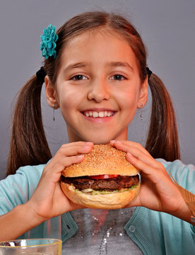 Retrato de una niña comiendo hamburguesa y patatas fritas con refresco.