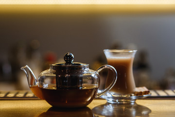 An underexposed lifestyle horizontal image of a teapot with hot alcoholic cocktail on a black tea basis. Wooden bar stand of a restaurant.