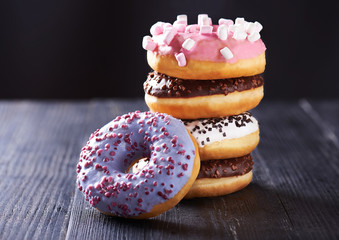 Close view at tasty donuts with blue, chocolate and vanilla icing on a dark wooden background. With copy space.