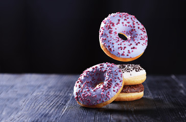Donut with blue icing in motion falling on a tasty donuts with chocolate and vanilla icing on a dark wooden background.