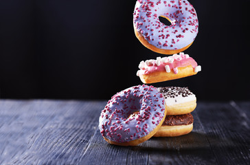 Donut with pink icing and marshmallow in motion falling on a tasty donuts with blue, chocolate and vanilla icing on a dark wooden background.