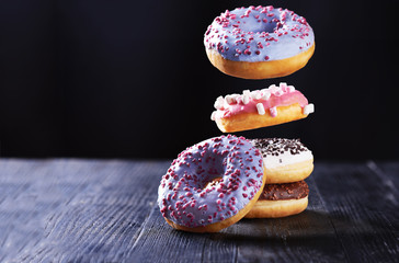 Donut with blue icing in motion falling on a tasty donuts with chocolate and vanilla icing on a dark wooden background.