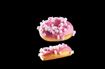 Two tasty donuts with pink icing and marshmallow in motion isolated on black