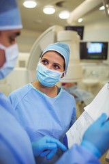 Male and female surgeons having discussion over clipboard