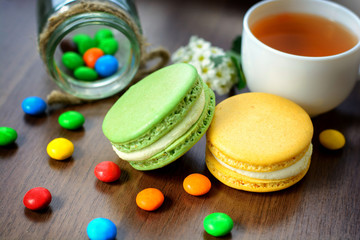 Colorful French macaroons and cup of tea on a rustic wooden background, selective focus