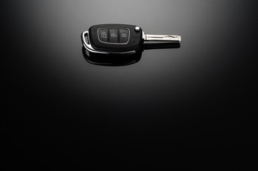 Modern car keys isolated on black reflective background with copy space for text or design elements. Folding key with remote alarm and trunk opening
