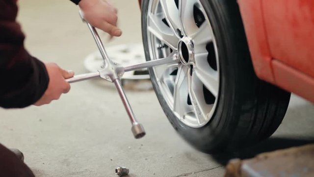 Car mechanic unscrewing car wheel of lifted automobile by wrench