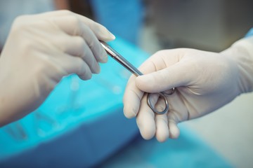 Surgeon passing surgical scissors to colleague